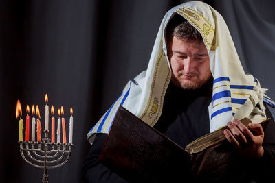 Man reading book while standing by illuminated candles on menorah