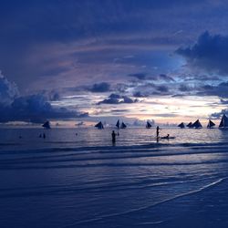 Silhouette people enjoying in sea against cloudy sky during sunset