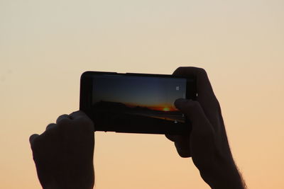 Close-up of hand holding smart phone against sky