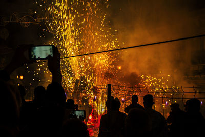 Silhouette people photographing firework display at night