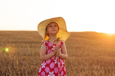 Adorable little girl in a straw hat pink summer dress in wheat field. child with long hair on sunset