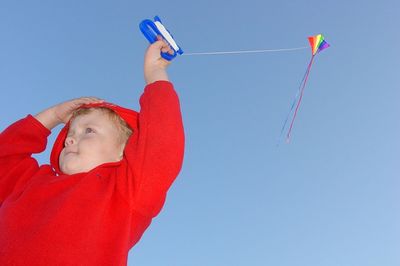 Low angle view of boy holding kite flying against clear sky