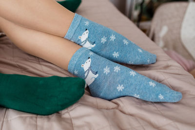 Low section of girl wearing sock relaxing on bed at home