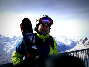 Portrait of man standing by railing against snow covered mountains and sky