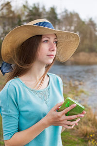 Beautiful young woman holding diary wearing hat while standing in forest