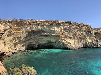 Rock formations by sea against clear blue sky