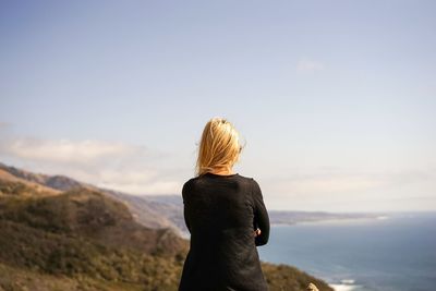 Rear view of woman looking at sea while standing on mountain against sky
