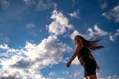 Low angle view of woman dancing against clouds in the blue sky 