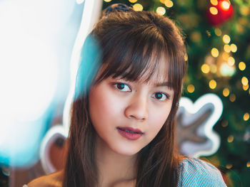 Portrait of young woman with illuminated christmas tree