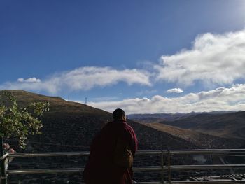 Rear view of man standing on mountain against sky