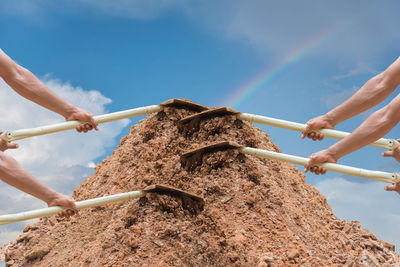 Multiple image of worker holding shovel on dirt heap against sky