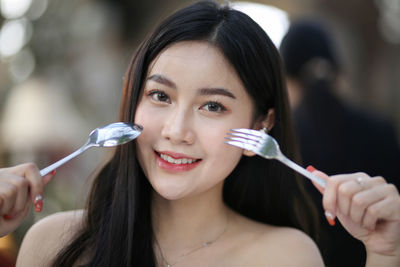 Close-up portrait of smiling woman holding spoon and fork