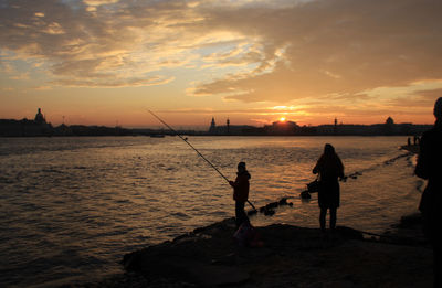 Silhouette people fishing in river against sunset sky