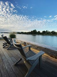 Empty chairs and table by swimming pool against sky