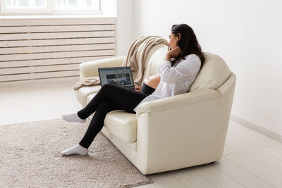 Woman using phone while sitting on sofa at home