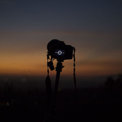 Close-up of silhouette camera against sky during sunset