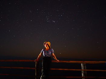 Woman standing on railing against sky at night