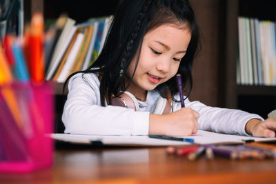 Close-up of girl writing on book at desk