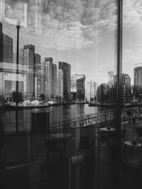 Digital composite image of modern buildings against sky seen through glass window