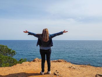 Rear view of woman with arms outstretched standing against sea