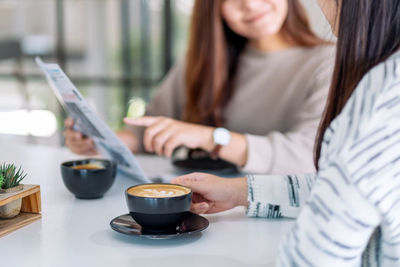 Midsection of female friends having coffee at table in cafe