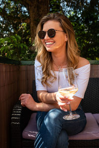 Young woman wearing sunglasses holding drink while sitting on chair