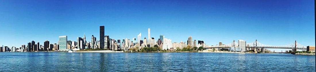 Panoramic view of sea in front of cityscape against clear blue sky