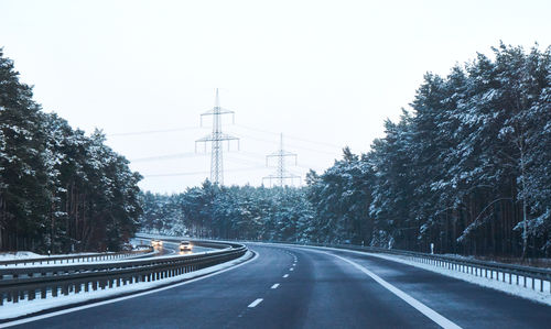 Empty road by trees against clear sky while winter