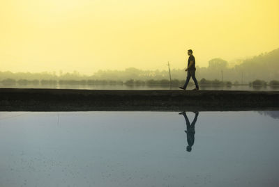 Silhouette man on lake against clear sky during sunset
