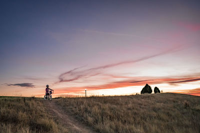 People riding bicycle on field against sky during sunset