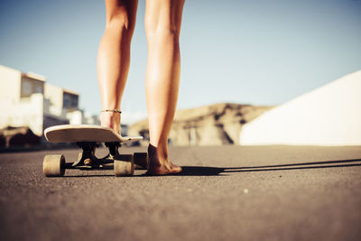 Low section of woman skateboarding against sky