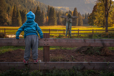 Rear view of boy standing on fence against field