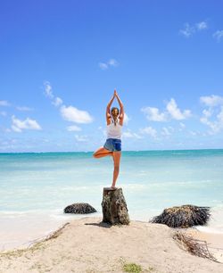 Rear view of woman standing on rock by sea against sky