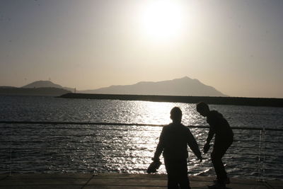 Silhouette people standing by sea against sky