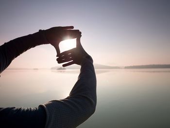 Fingers gesturing picture frame on sunrise seaside. sunlight on beach. sunset at the sea. hand frame