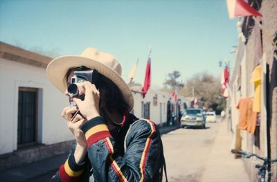 Young man photographing while standing against sky on sunny day