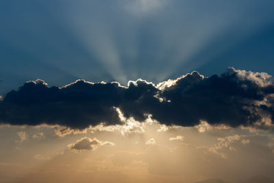 Low angle view of sunlight streaming through clouds