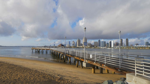 Pier on beach against cloudy sky