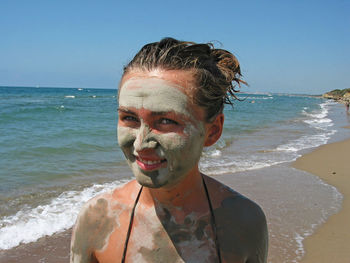 Portrait of woman wearing mud mask at beach against clear sky