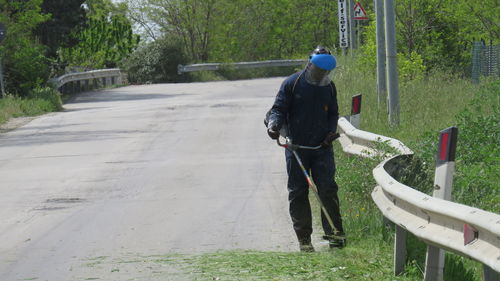 Worker cutting grass with brush cutter by road