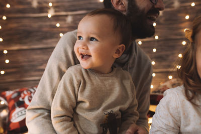 Baby boy smiling with his dad in living room decorated by christmas tree and present gift box