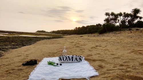 Information sign on sand at beach against sky during sunset
