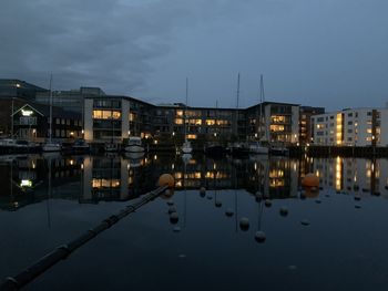 Illuminated buildings by lake against sky at dusk