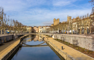 Bridge over river by buildings against sky