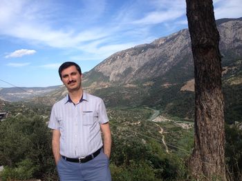 Portrait of young man standing on mountain against sky