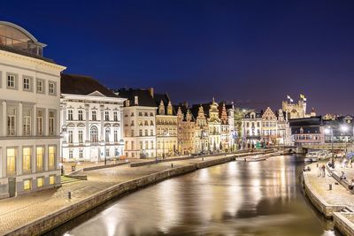 Illuminated buildings by river against sky in city at night