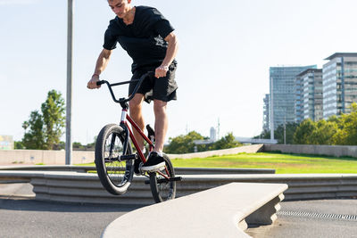 Crop young male riding bmx bike on edge of border on sunny weekend day on city street in summer