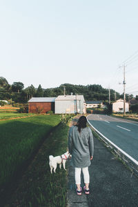 Rear view of man standing with dog against clear sky