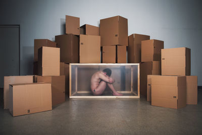 Naked mid adult man sitting in container by cardboard boxes at home