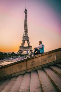 Side view of man sitting against eiffel tower and dramatic sky in city